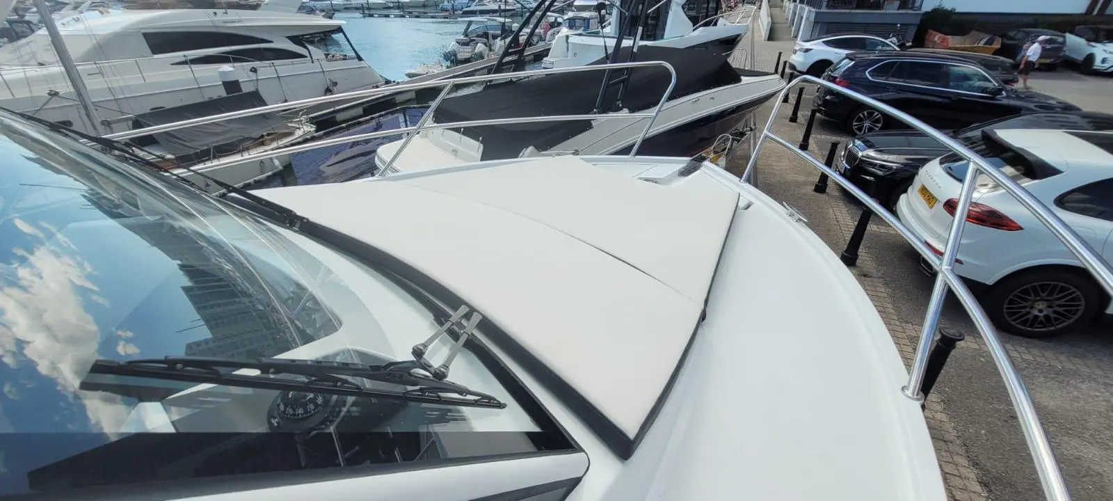 View from the bow of a luxury yacht, showing nearby boats and parked cars in a marina setting.